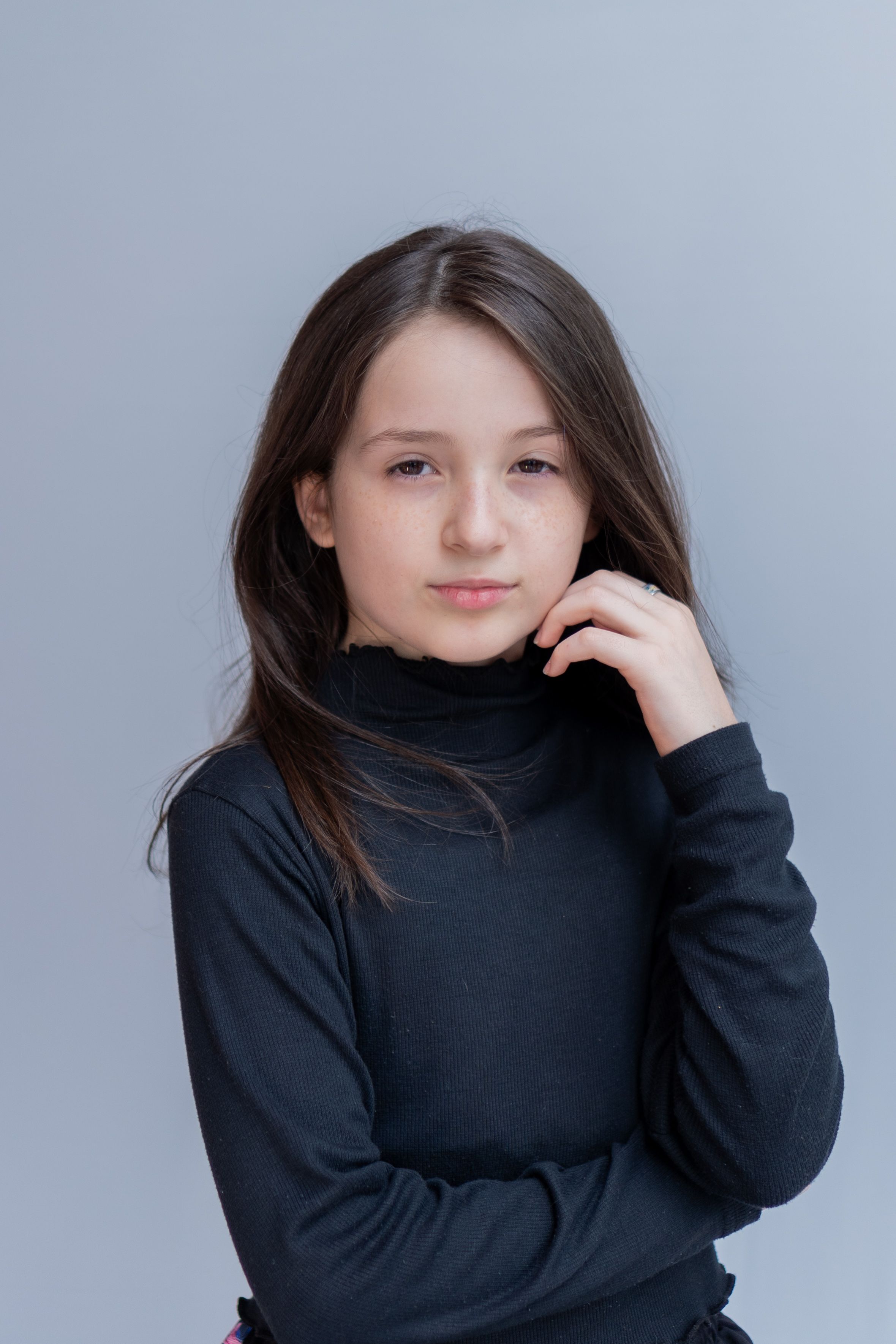 A confident young girl posing against a neutral background, exuding elegance in a black turtleneck.