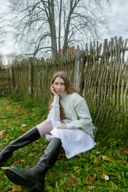 Young woman in cozy attire relaxes by a rustic fence in autumn