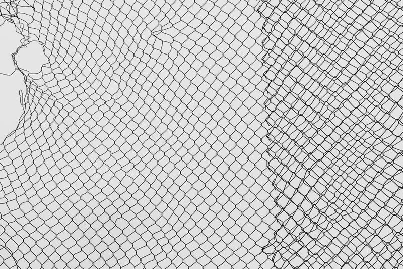 A close-up view of a torn, black safety net with intricate patterning against a white background.