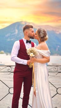 A couple sharing a kiss by a picturesque lake during sunset, celebrating their wedding.