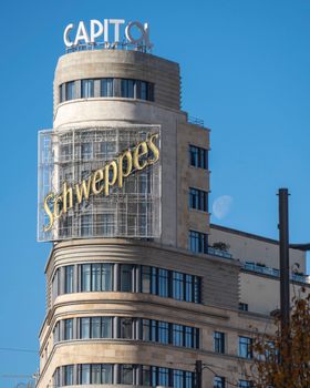 Iconic Capitol Building with Schweppes sign in Madrid, Spain against a clear blue sky.