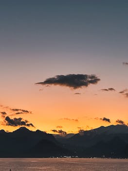 A breathtaking sunset over a peaceful mountain range with calm waters beneath.