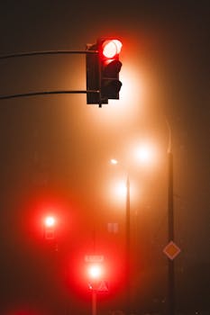 Eerie city nightscape featuring glowing red traffic lights in the mist.