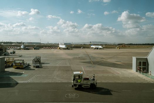 Wide view of an airport tarmac with multiple airplanes and ground vehicles under a cloudy sky.