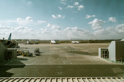 View of airport terminal and runway with planes under a cloudy sky.