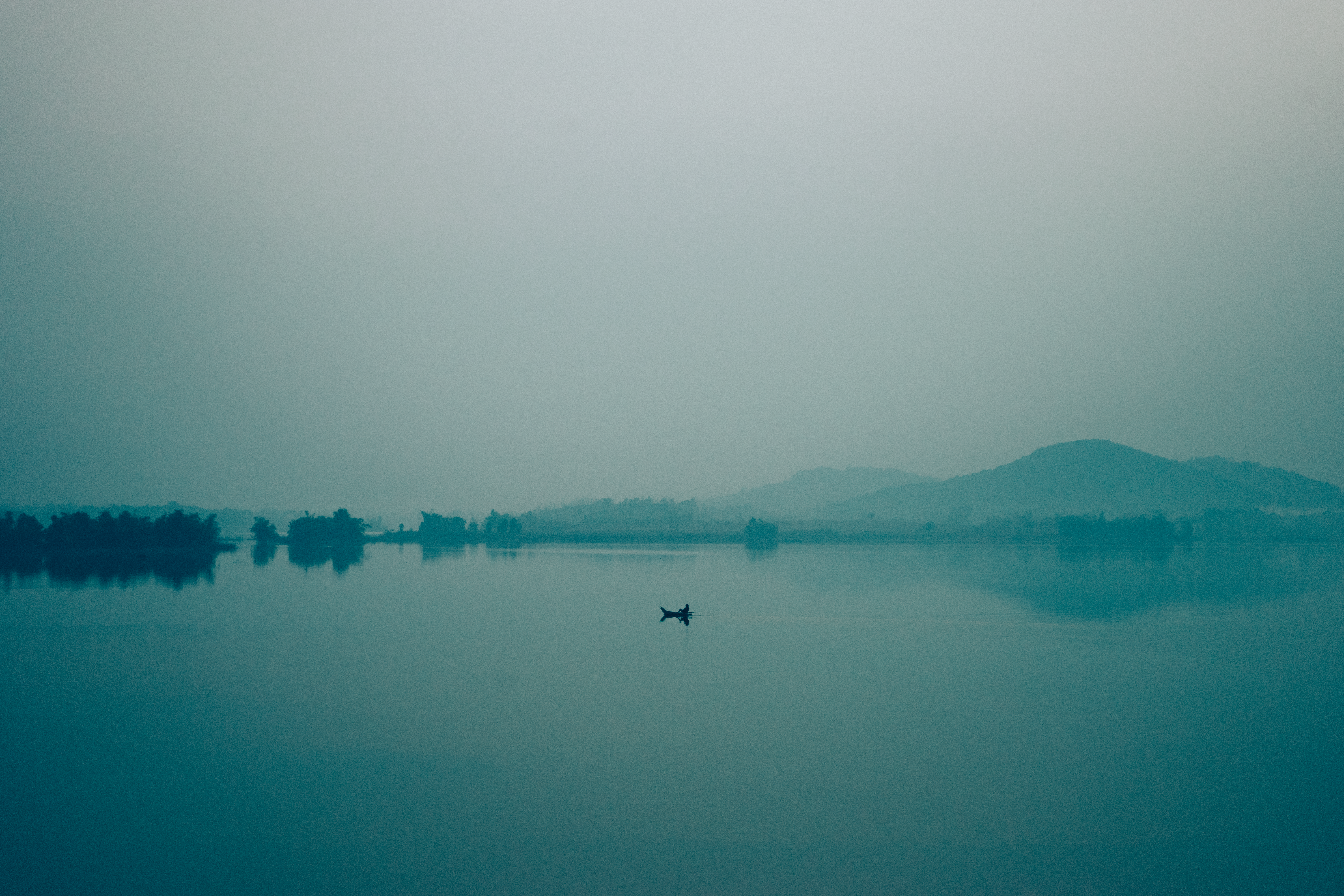 A lone boat on Tây Lake in Hà Nội, captured in a tranquil, misty morning setting.
