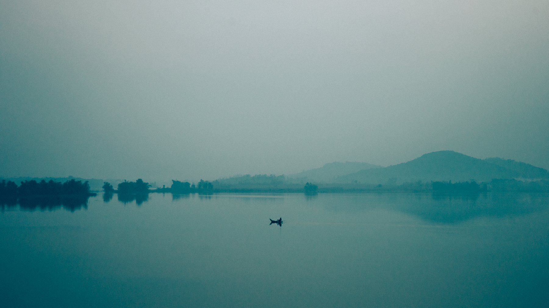 A lone boat on Tây Lake in Hà Nội, captured in a tranquil, misty morning setting.