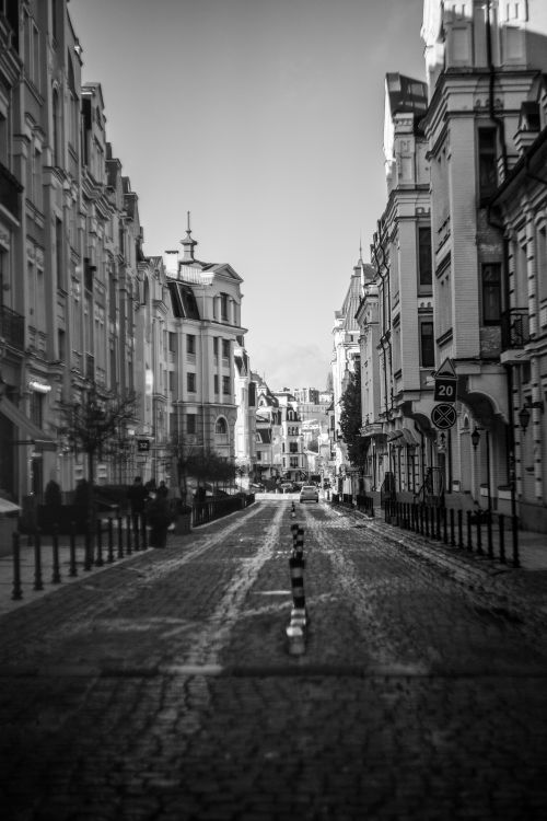 Free Black and white photo of a cobblestone street lined with historic buildings in a European city. Stock Photo