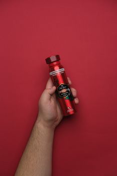 A hand holding a red Old Spice deodorant bottle against a red background, emphasizing freshness and masculinity.