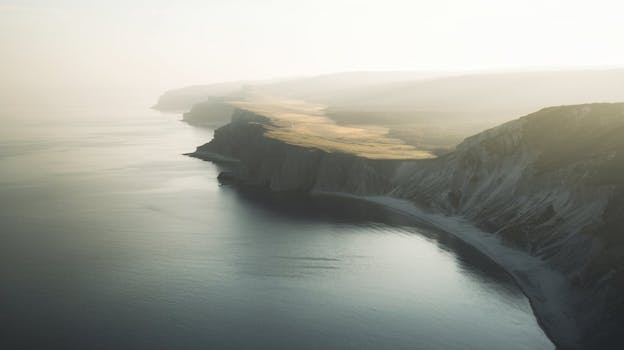A tranquil aerial view of misty cliffs and calm ocean waters during sunrise