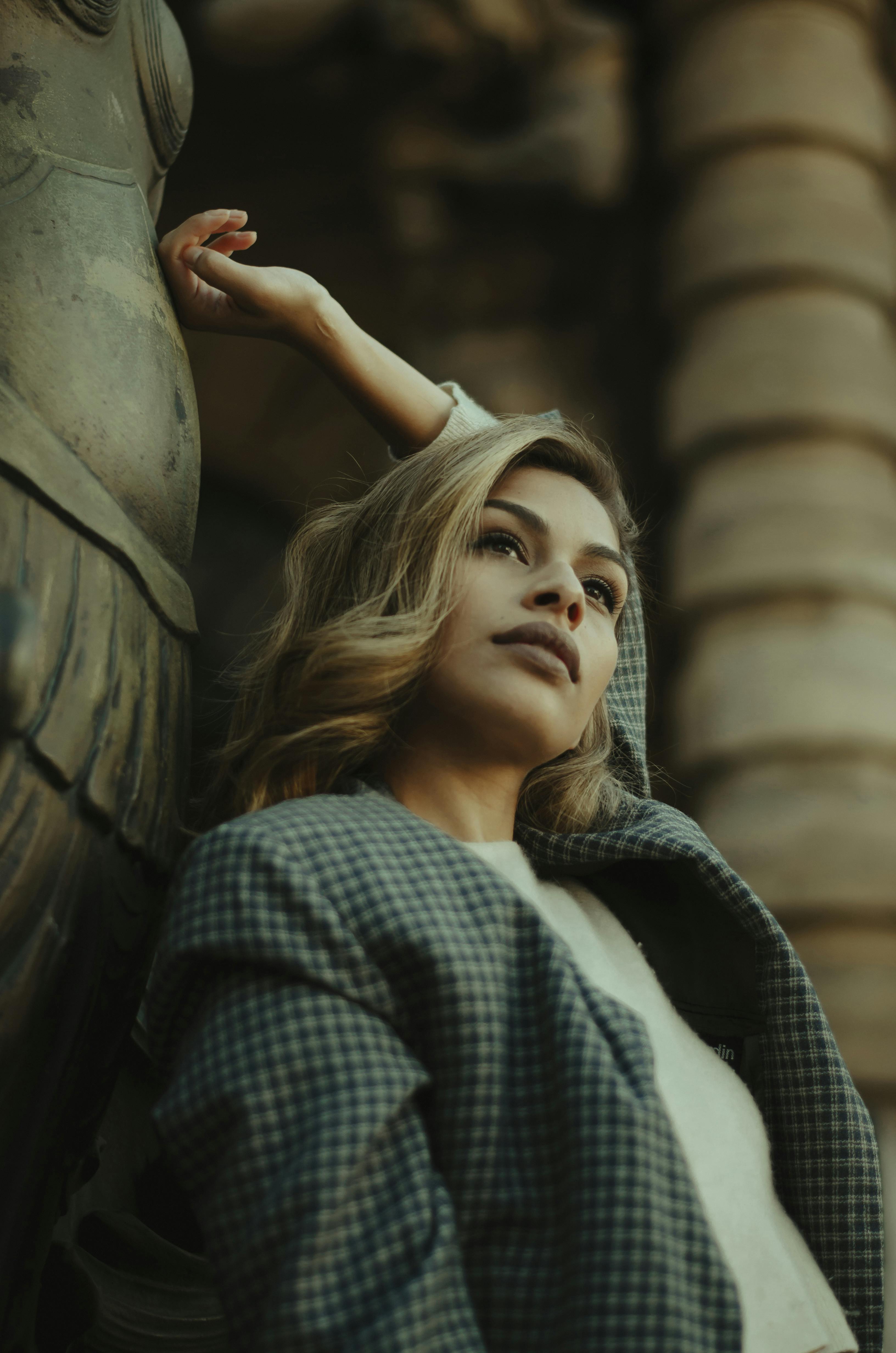 Stylish woman in plaid coat poses gracefully by a grand statue, evoking elegance and confidence.