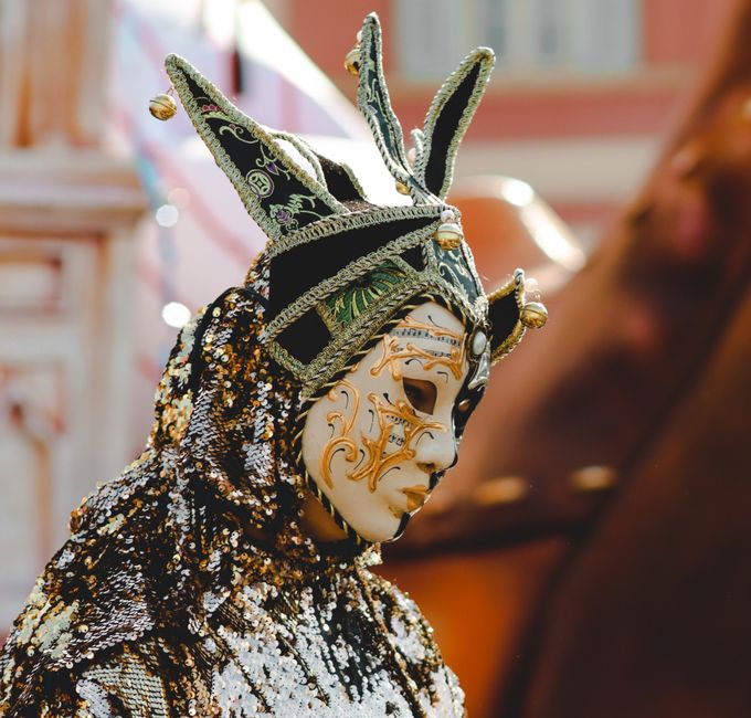 Colorful jester-style mask with intricate designs worn at a festive Venice carnival.