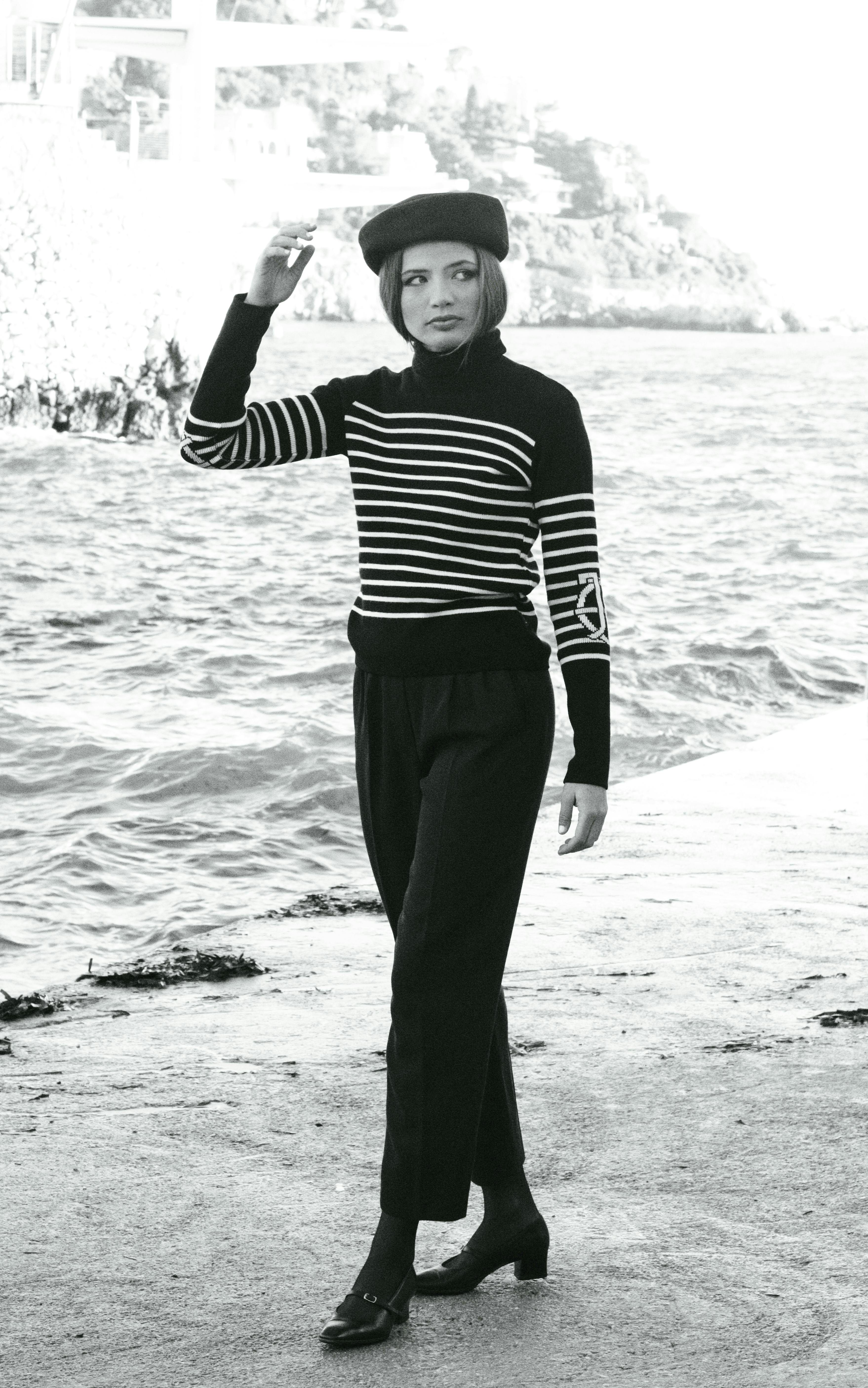 bezplatná Stylová žena v pruhovaném svetru a baretu se prochází u moře a vyzařuje z ní vintage kouzlo. Základová fotografie