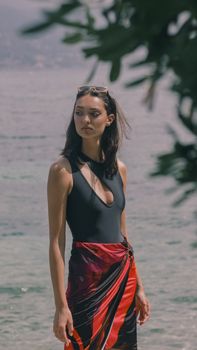 A stylish woman in swimwear enjoys a sunny day by the beach, exuding a calm and elegant demeanor.