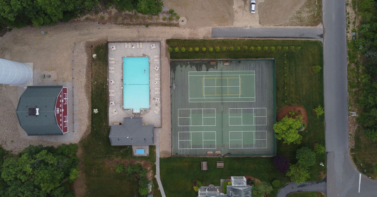 Drone shot of tennis courts, pool, and surrounding greenery in a residential area for sports and leisure.