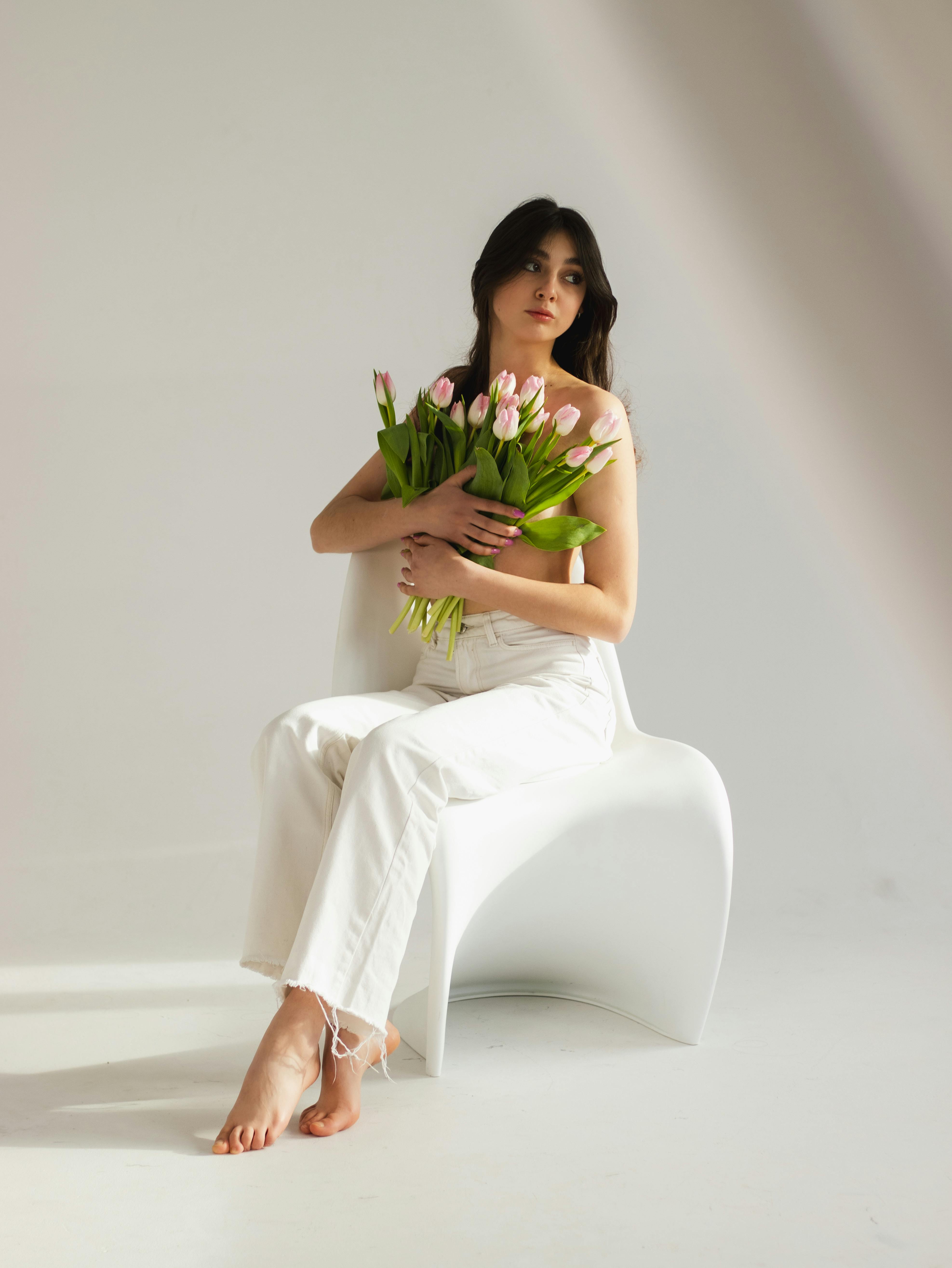 Elegant woman in white holding tulips, captured in a minimalist setting with soft lighting.