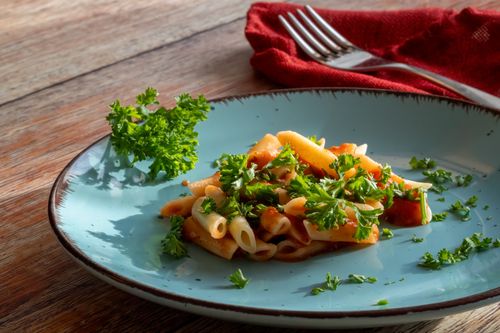 Free Delicious penne pasta topped with fresh parsley and tomato sauce on a blue plate. Stock Photo