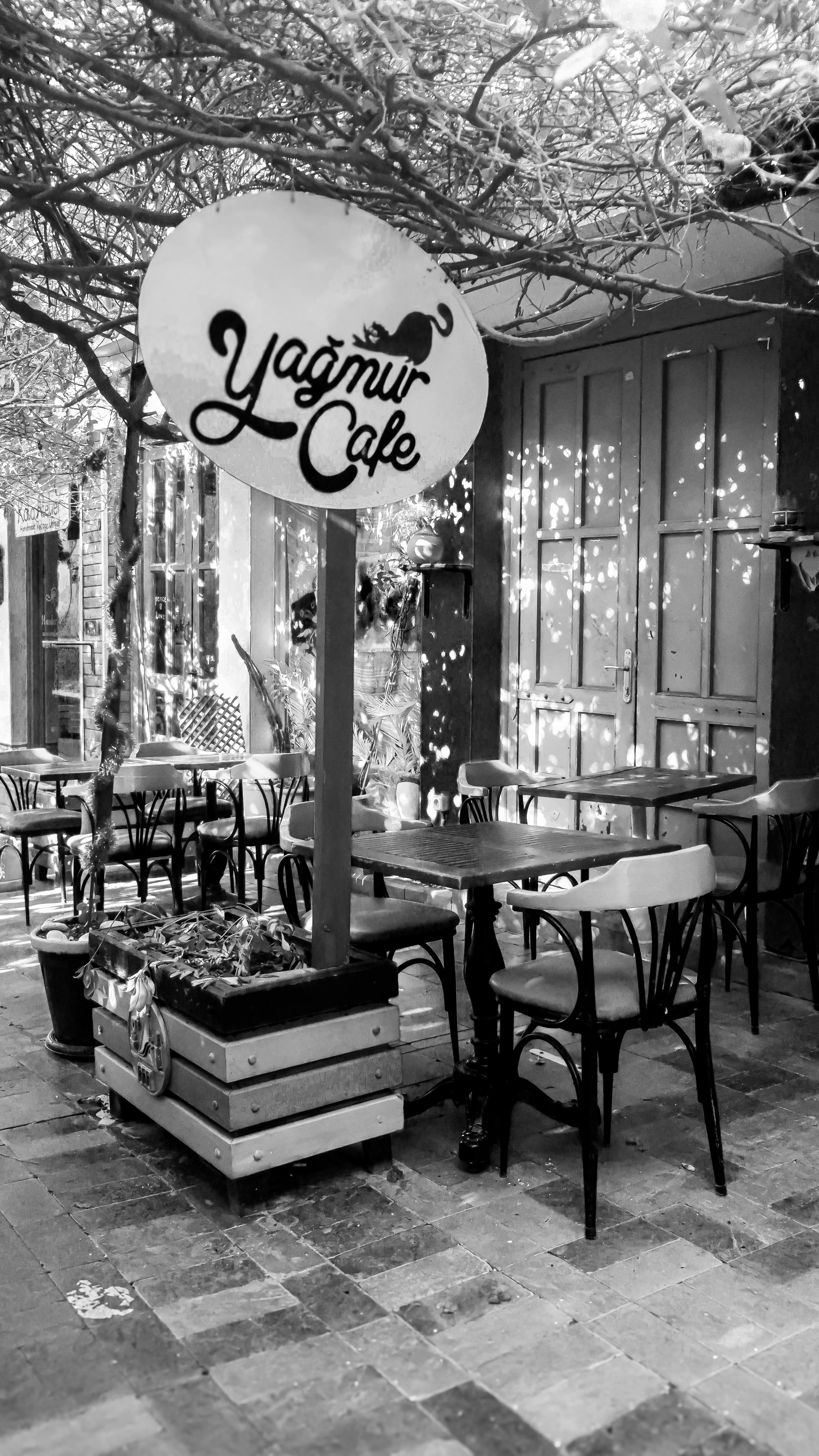 Black and white image of a quaint outdoor café with rustic charm and empty seating.