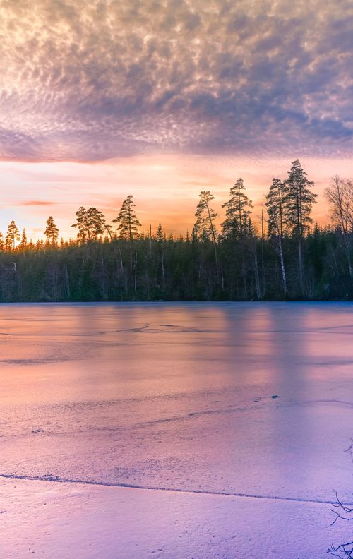 Free Tranquil winter scene of a frozen lake with sunset colors reflecting on the ice. Stock Photo