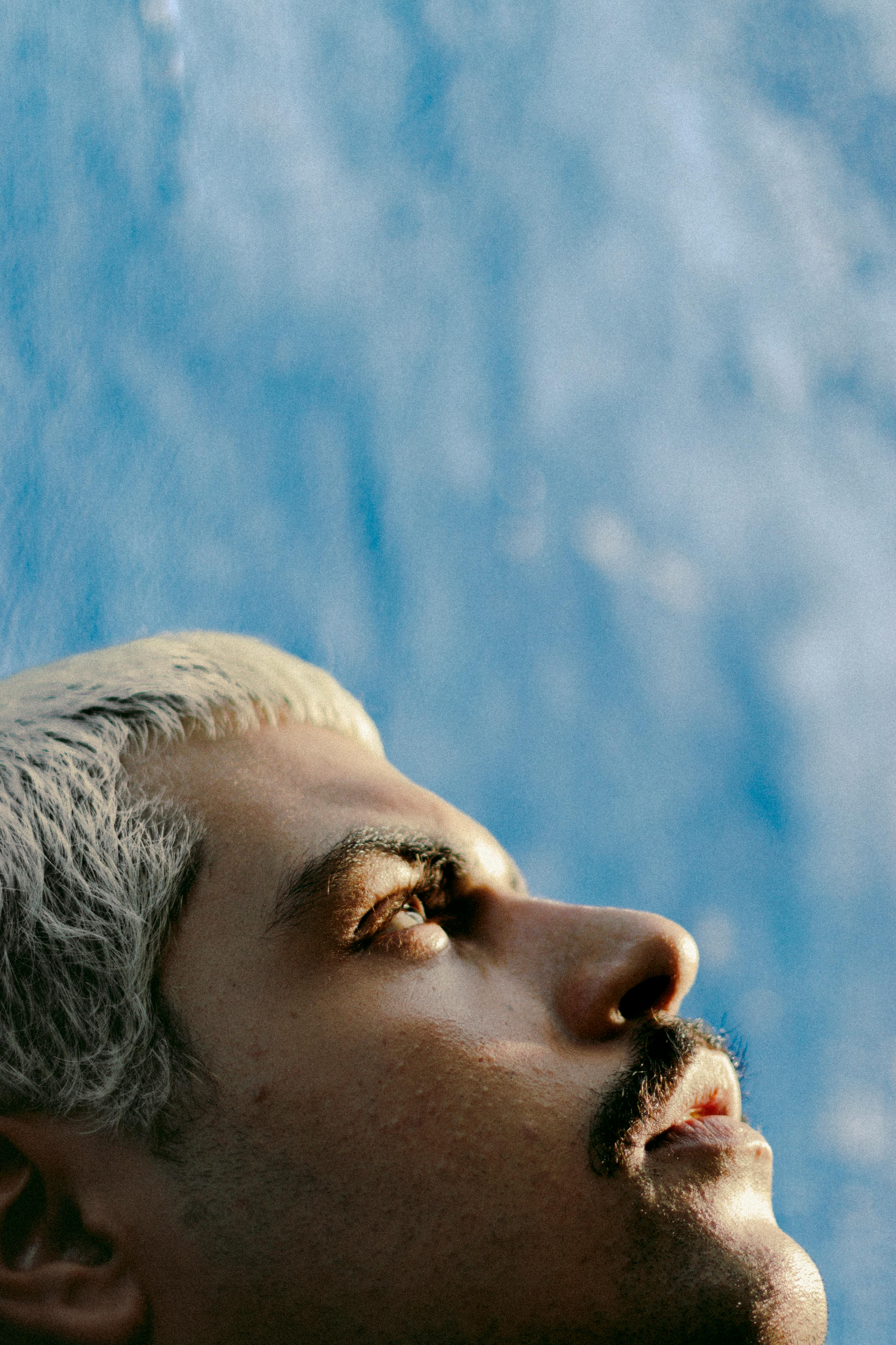 Close-up of a contemplative adult male looking upward against a blue background.