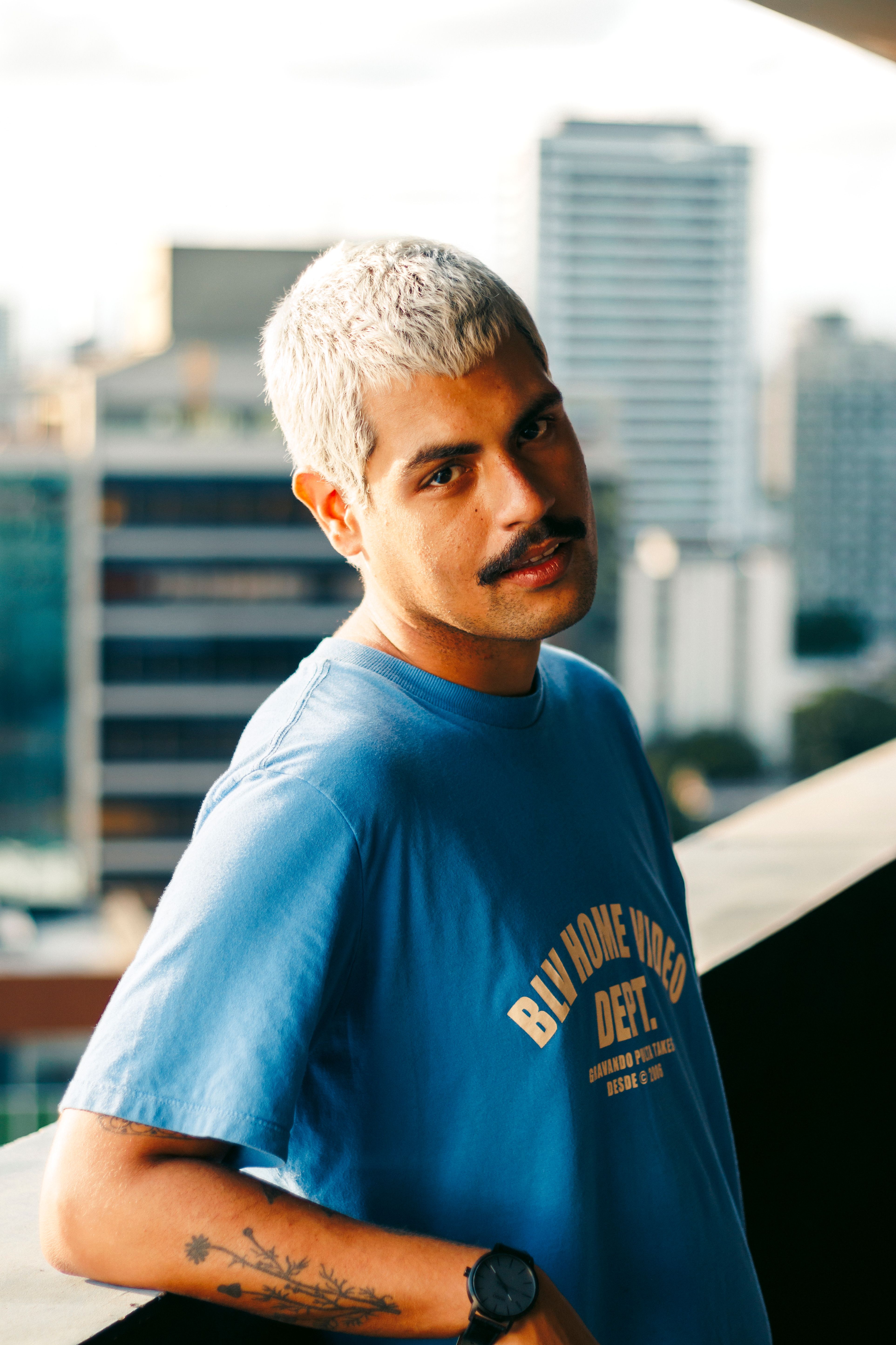 A man with short hair and mustache posing in a vibrant urban background.