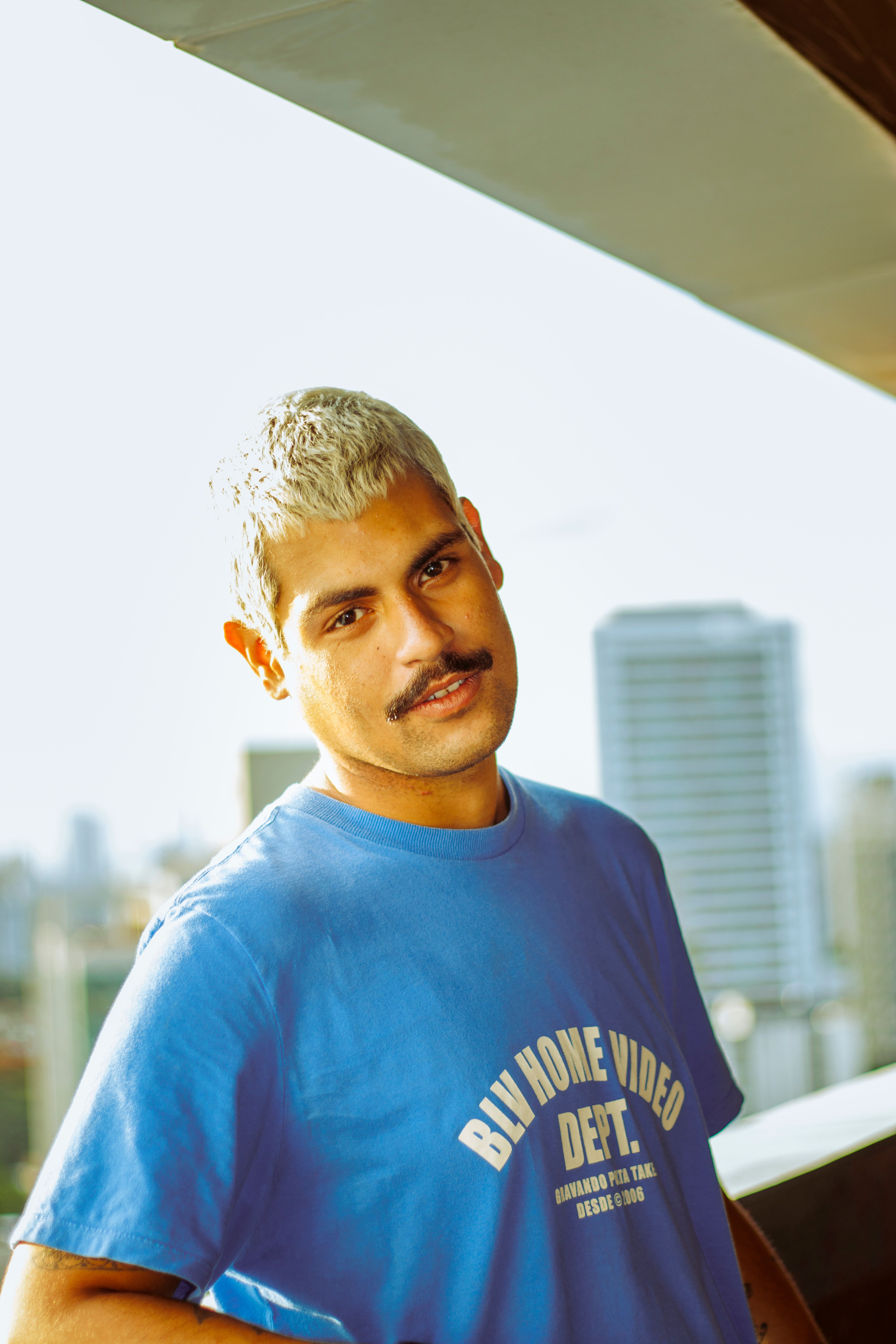 Confident young man with mustache wearing blue shirt, urban background.