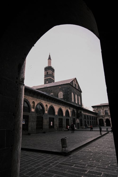 Free Historic Diyarbakir Great Mosque framed by arch. People walk in courtyard. Stock Photo