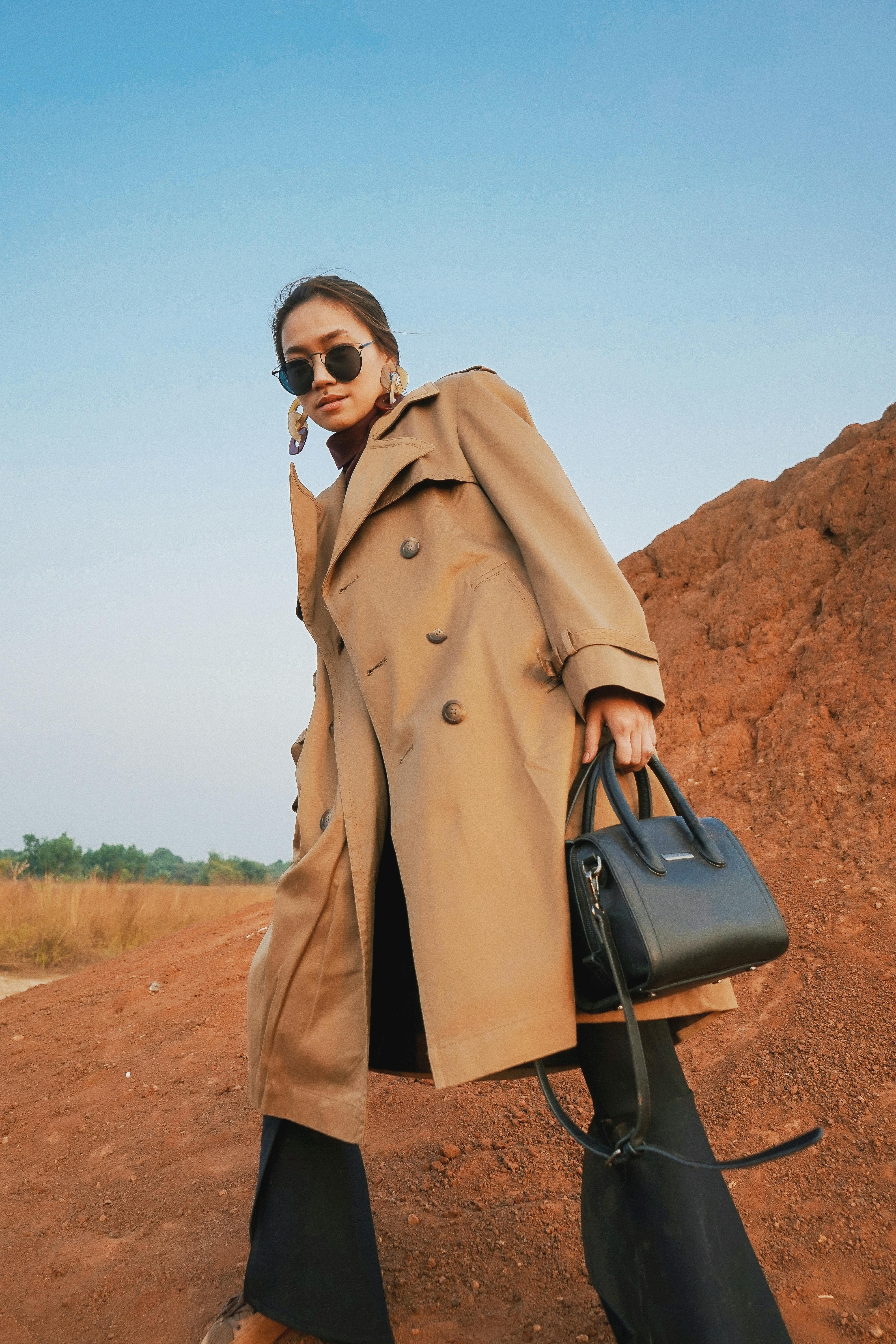 一位时尚女性穿着风衣、戴着太阳镜，在户外以蓝天为背景合影