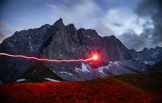 A long exposure captures a mystical red light streak against the majestic Alps at night, revealing a sense of mystery and adventure.