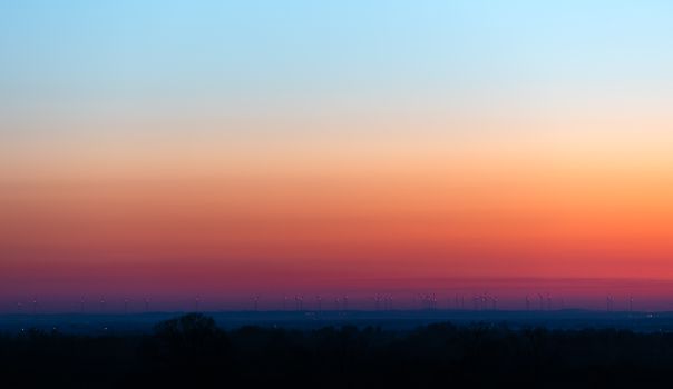 A stunning view of a wind farm silhouetted against a colorful sunset sky in Poland.