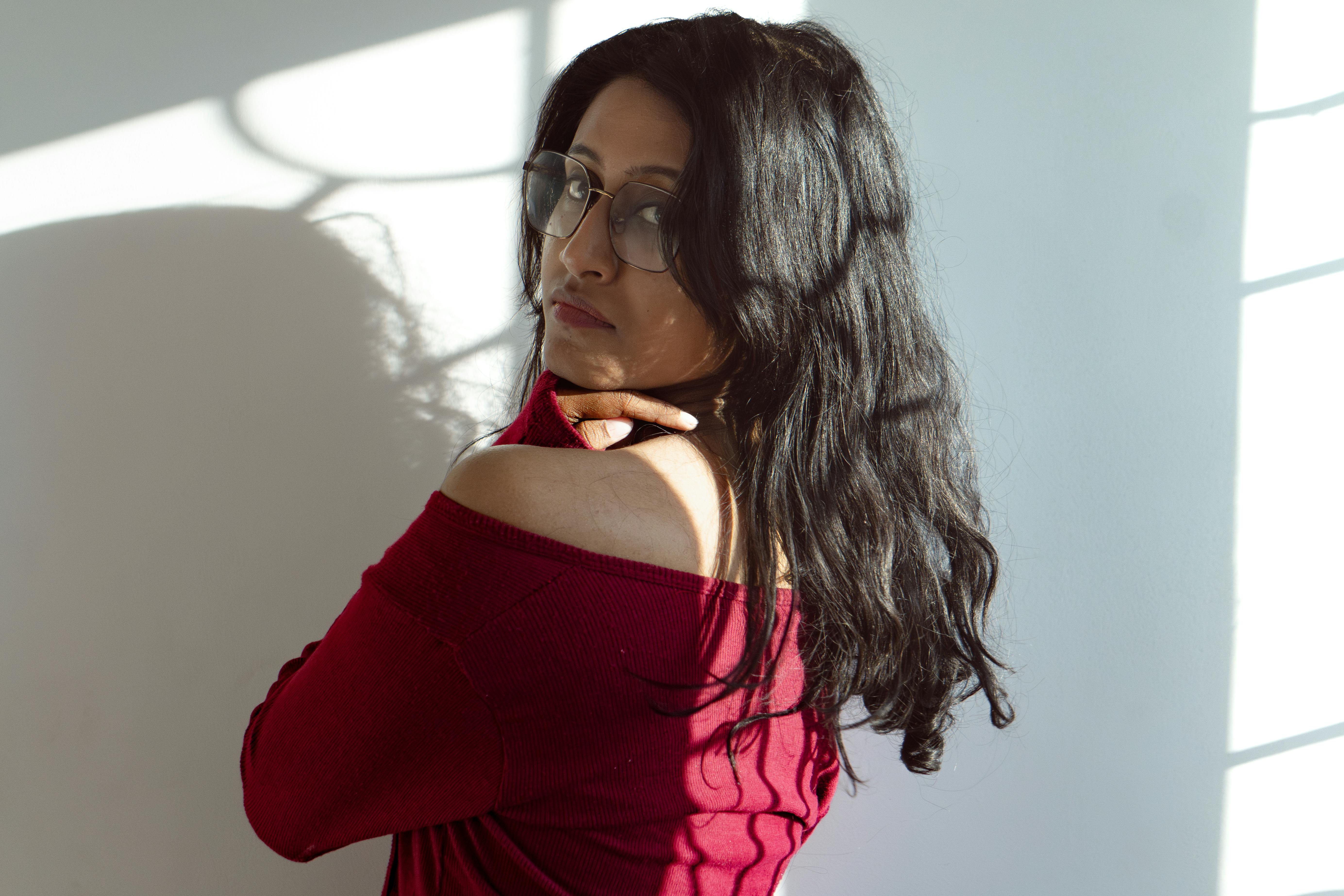 A woman in a red sweater poses gracefully with shadows on the wall in a sunlit room.
