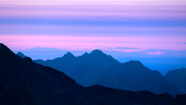 Majestic view of a mountain range at sunrise with hues of pink and blue, perfect for nature lovers.