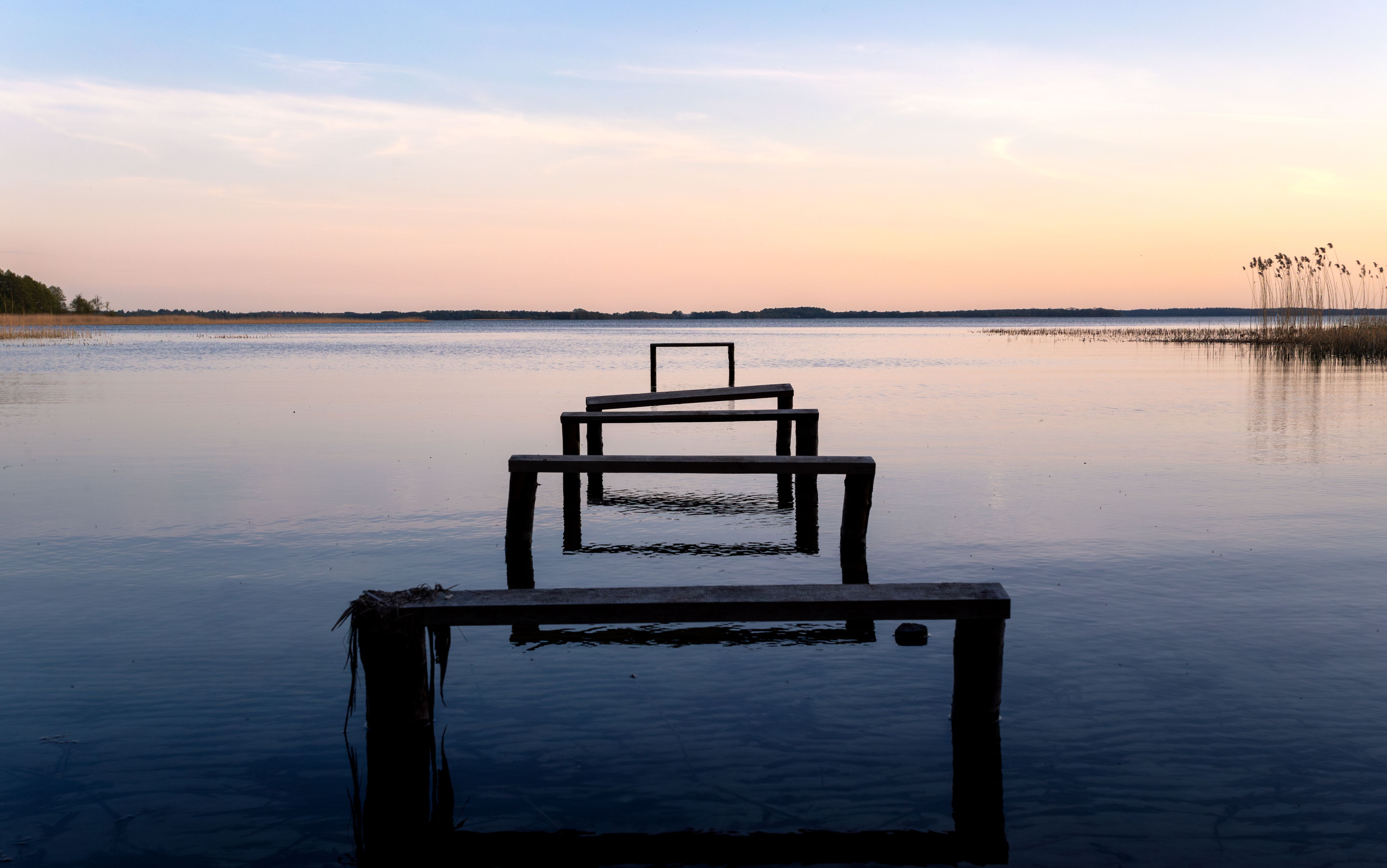 Calm evening at a lake with a wooden pier and serene sunset glow.