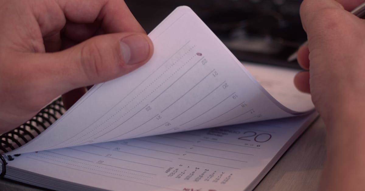 Hands flipping through a planner with a laptop in the background, depicting organization