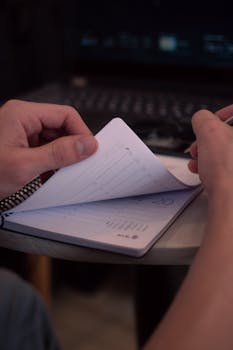 Hands flipping through a planner with a laptop in the background, depicting organization