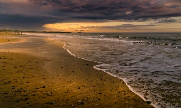 A serene beach at sunset with waves and a dramatic sky.