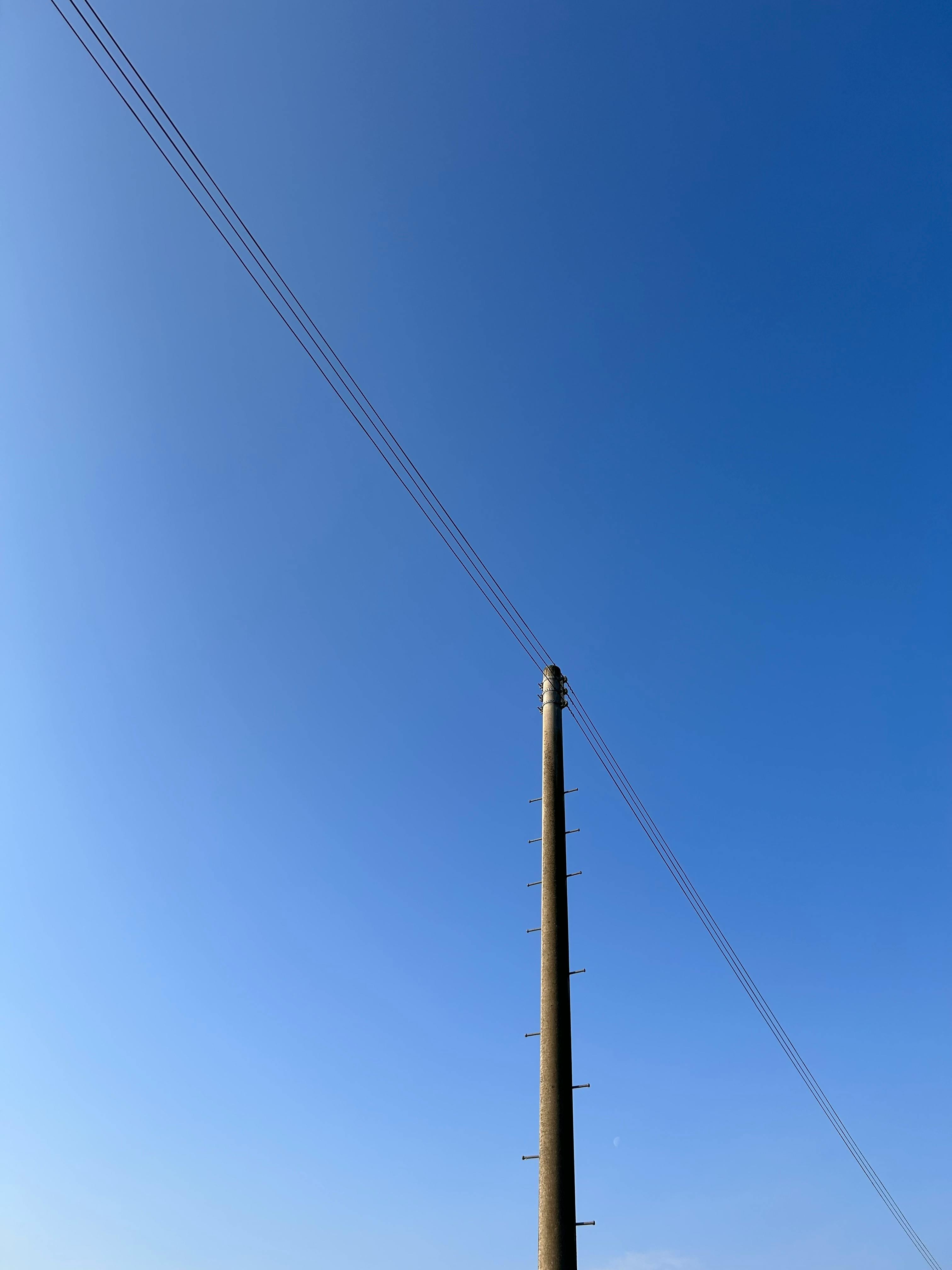 Kostnadsfria En ensam kraftledning står högt mot en klarblå himmel och visar upp enkelheten. Stock foto