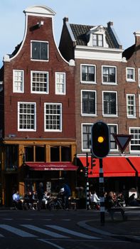 Sunny day in Amsterdam showcasing iconic Dutch gabled houses and street cafe.