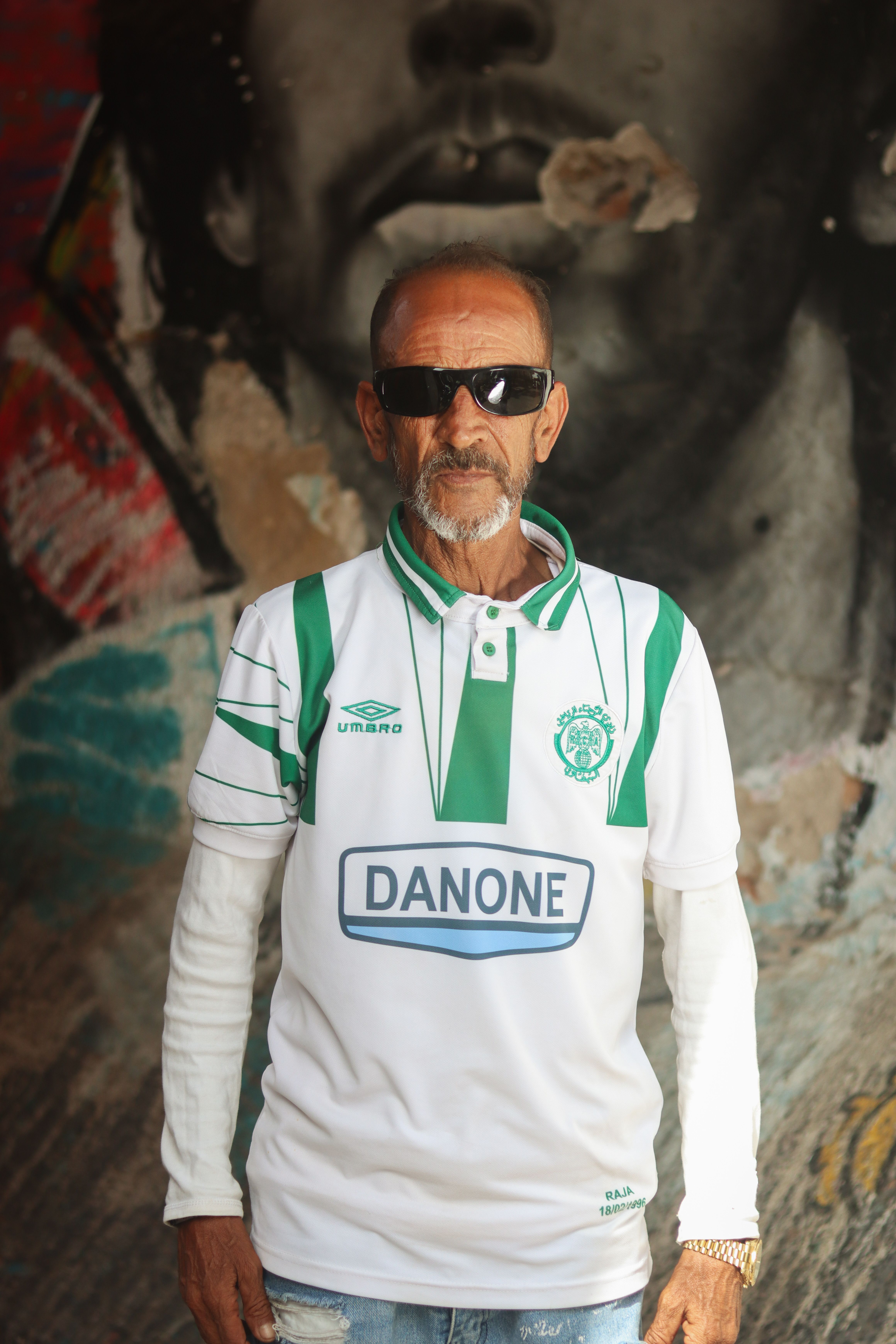 Senior man in Casablanca with sunglasses and football shirt in front of artistic mural.