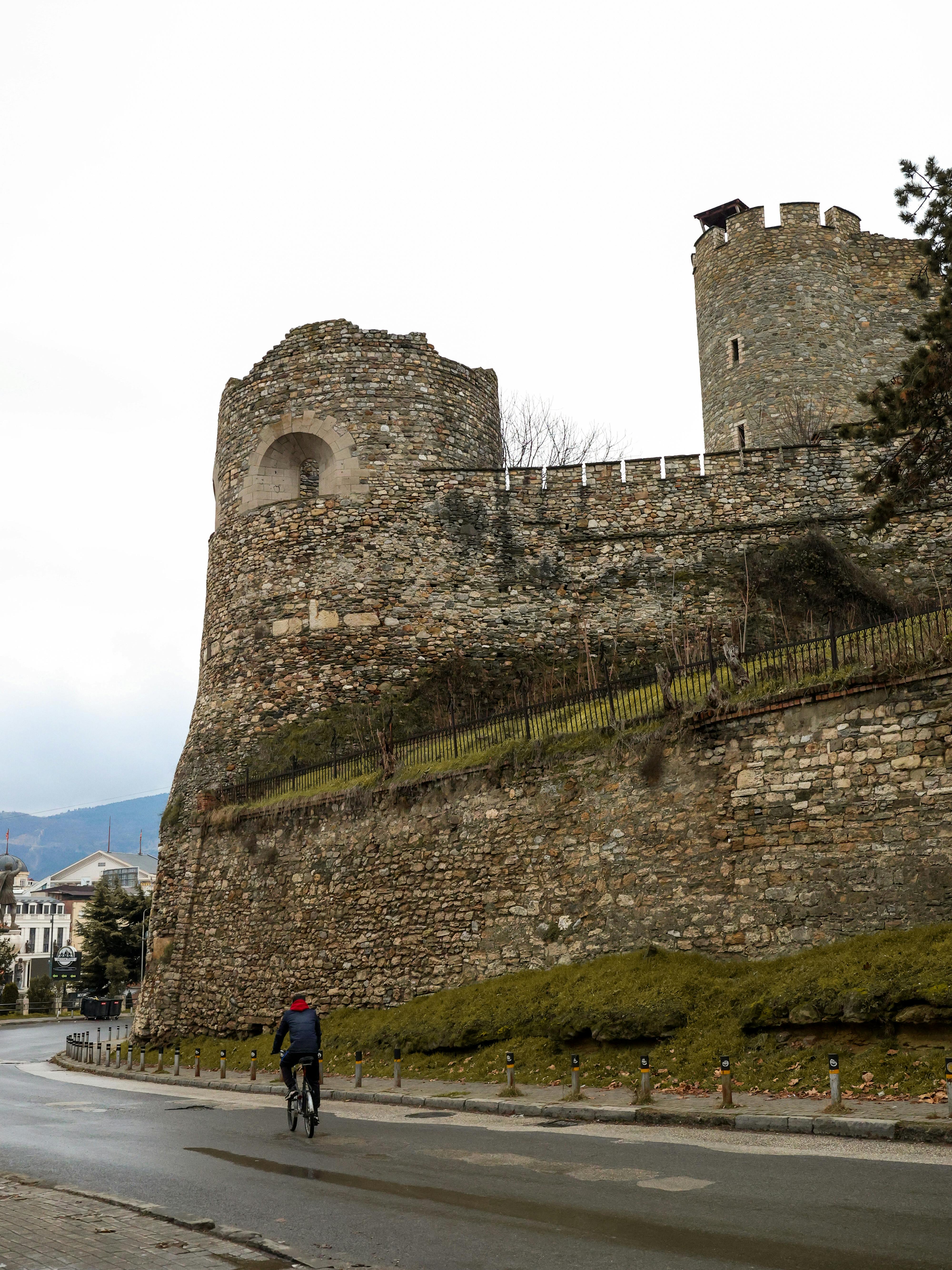 A cyclist rides near a historic stone fortress in Macedonia on a cloudy day.