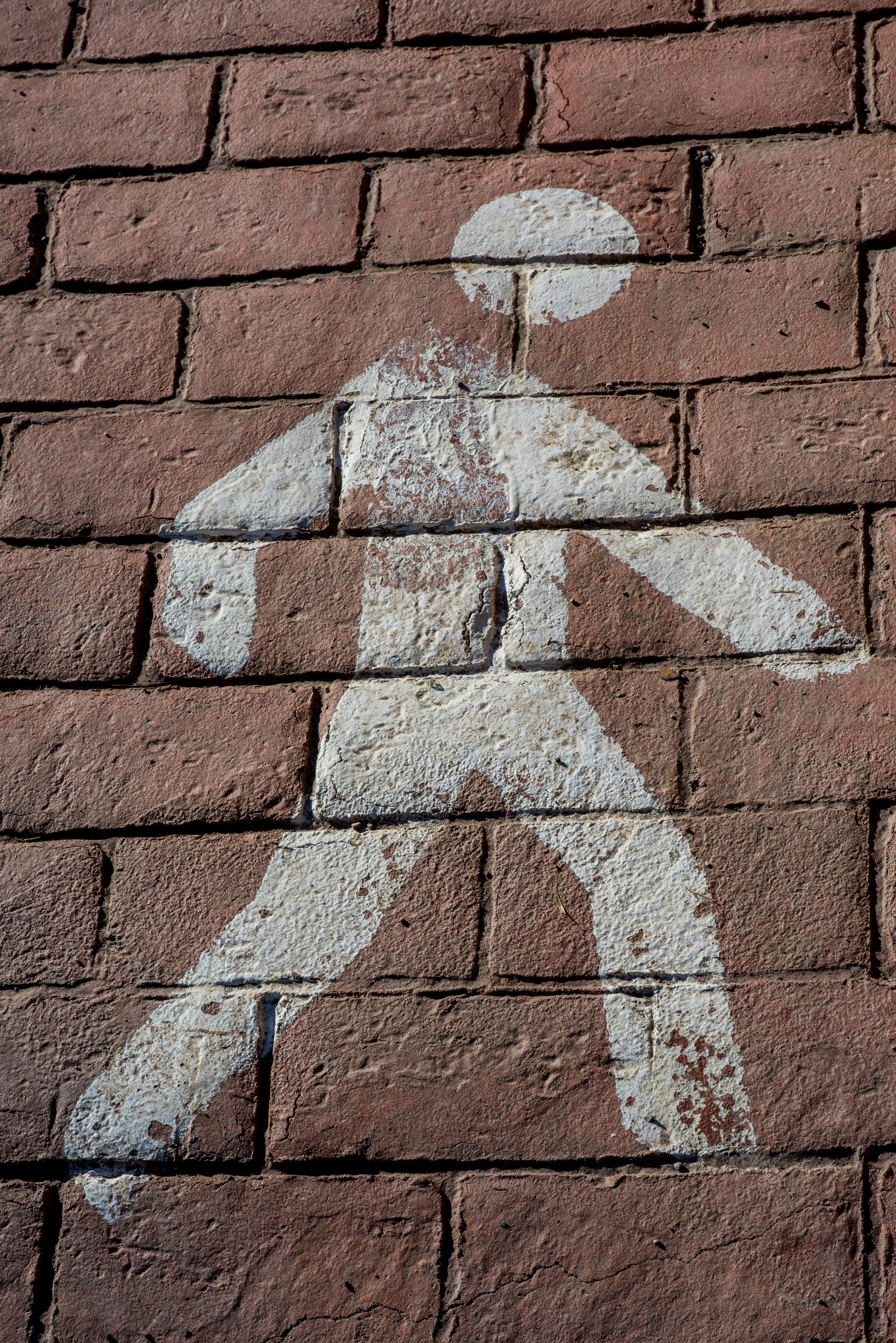 Close-up of a weathered pedestrian symbol painted on a red brick wall.