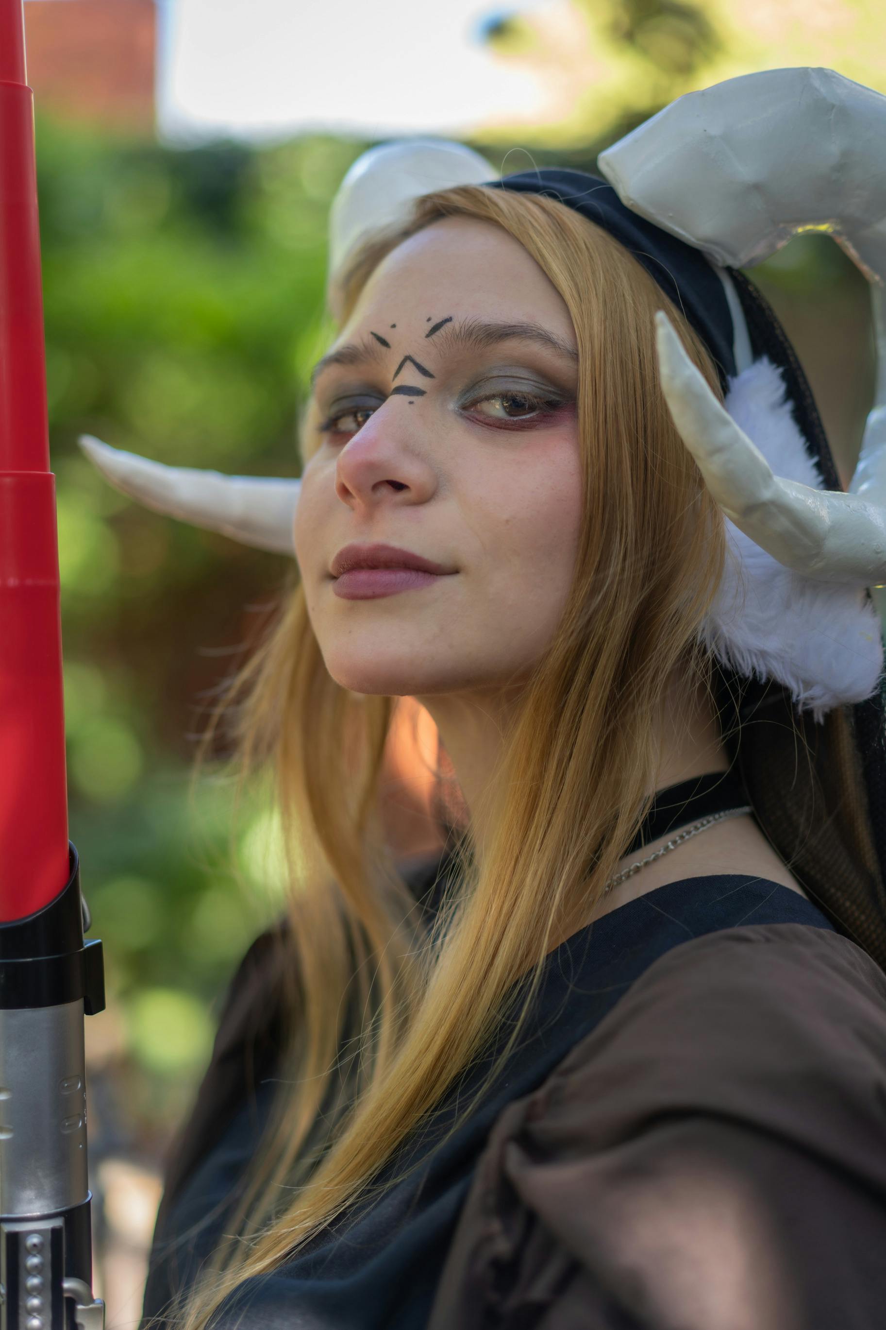 Female cosplayer in fantasy costume with horns and lightsaber at Buenos Aires convention.