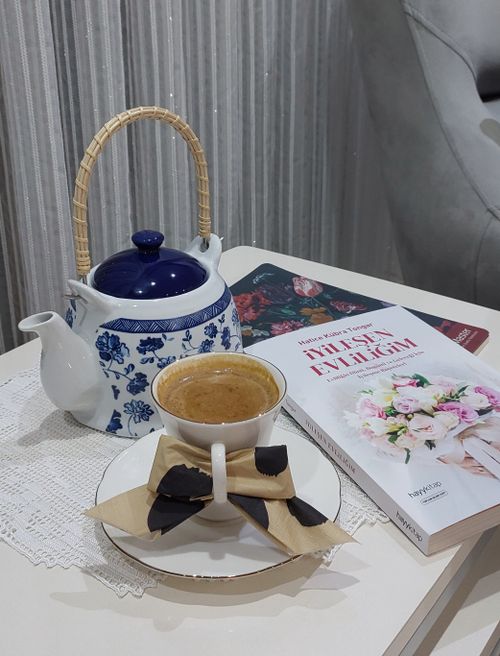 Free A cozy tea setup with a floral teapot, decorative cup, and book on a lace tablecloth. Stock Photo