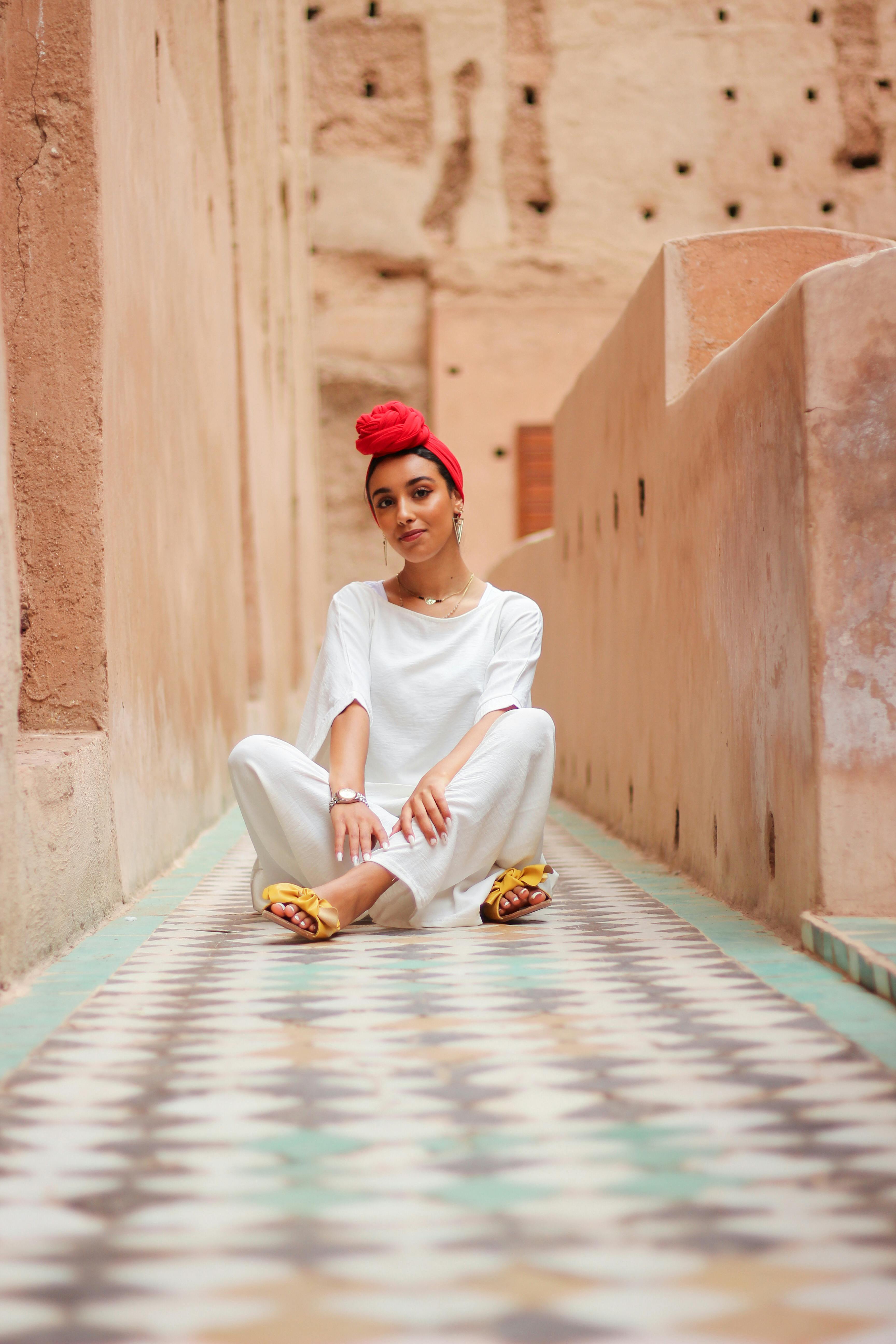 Portrait of a woman sitting in a Marrakech alley wearing traditional Moroccan attire with a red turban.