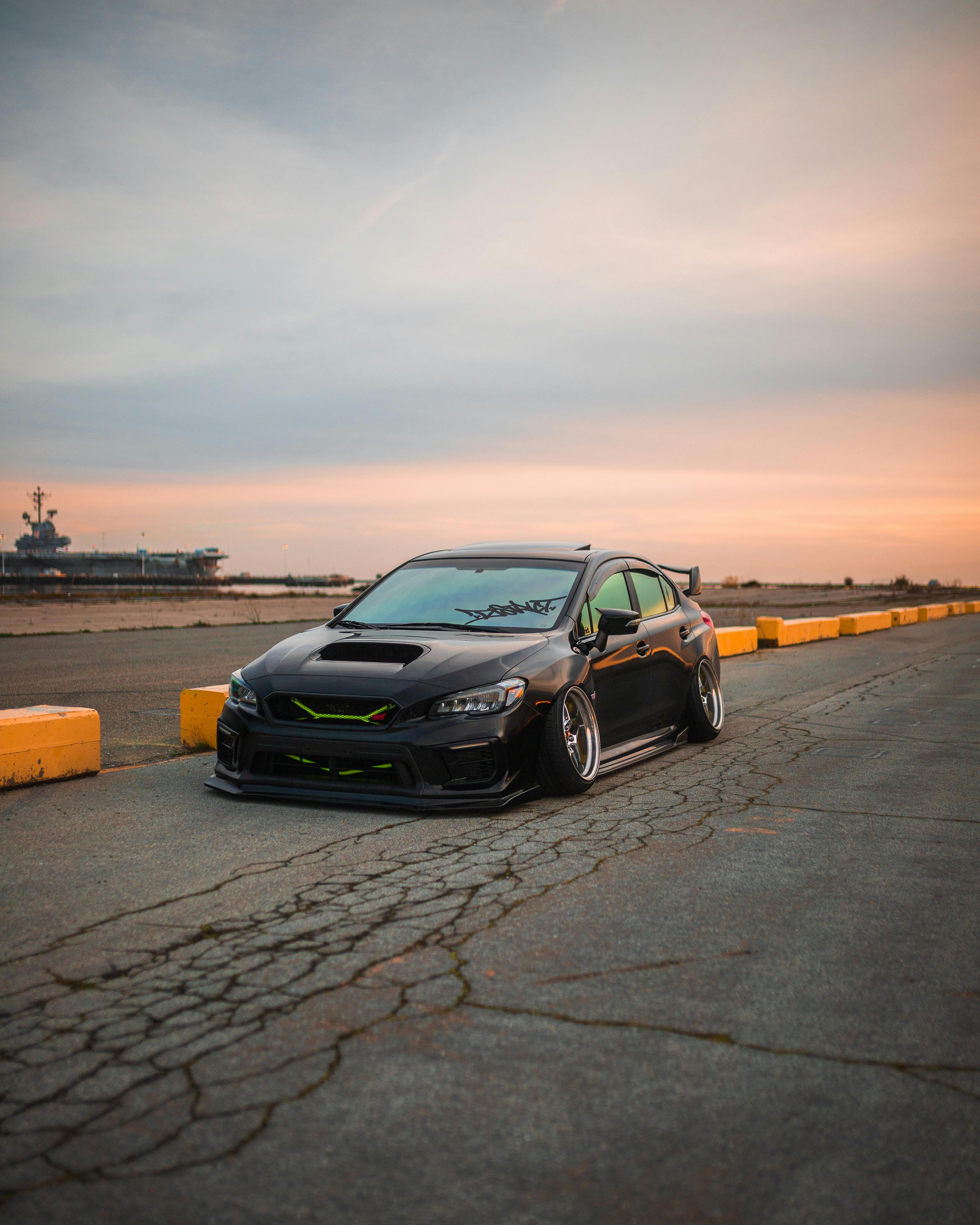 bezplatná Upravené černé auto zaparkované na prázdné nábřežní silnici při západu slunce, předvádějící městský styl a klid. Základová fotografie