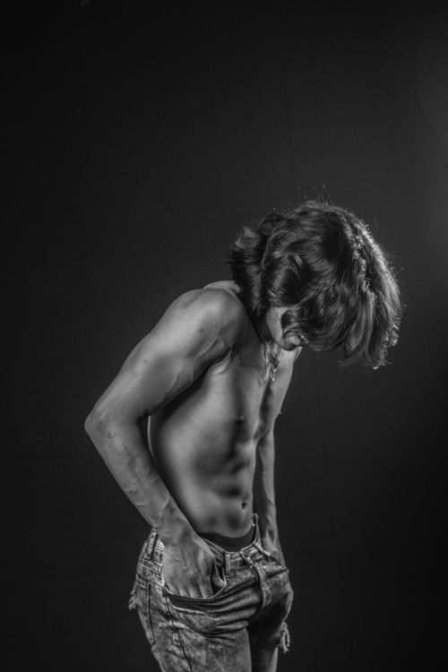 Free Black and white portrait of a young man with long hair posing shirtless, looking down. Stock Photo