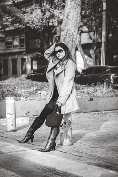 Stylish woman in trench coat and boots posing confidently on city street.