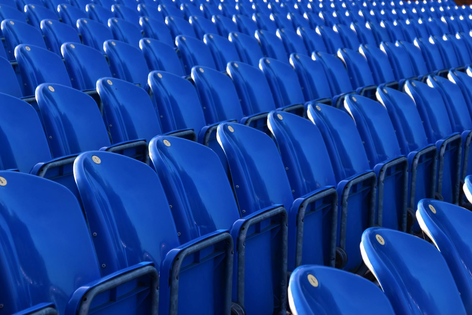 Rows of blue plastic seats in a vacant outdoor stadium on a sunny day.