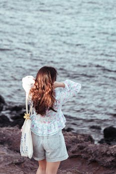 Young woman photographing the ocean on a rocky shore.