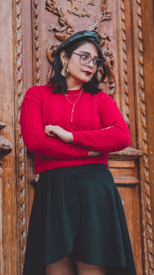 Free Fashionable woman in red sweater and skirt, posing against ornate wooden door. Stock Photo